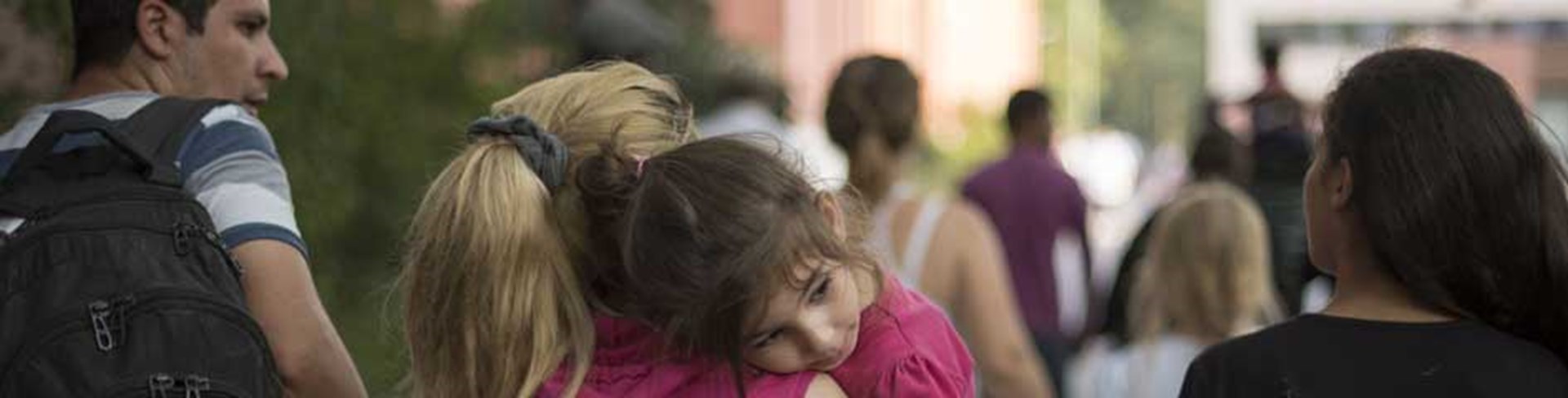 Eine Frau trägt ein Kind auf dem Arm, rechts daneben eine Frau von hinten, links ein Mann