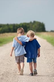 Zwei kleine Jungs laufen Arm in Arm einen sandigen Weg entlang
