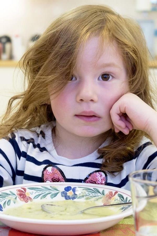 Kleines Mädchen mit Brot in der Hand vor einem Teller Suppe