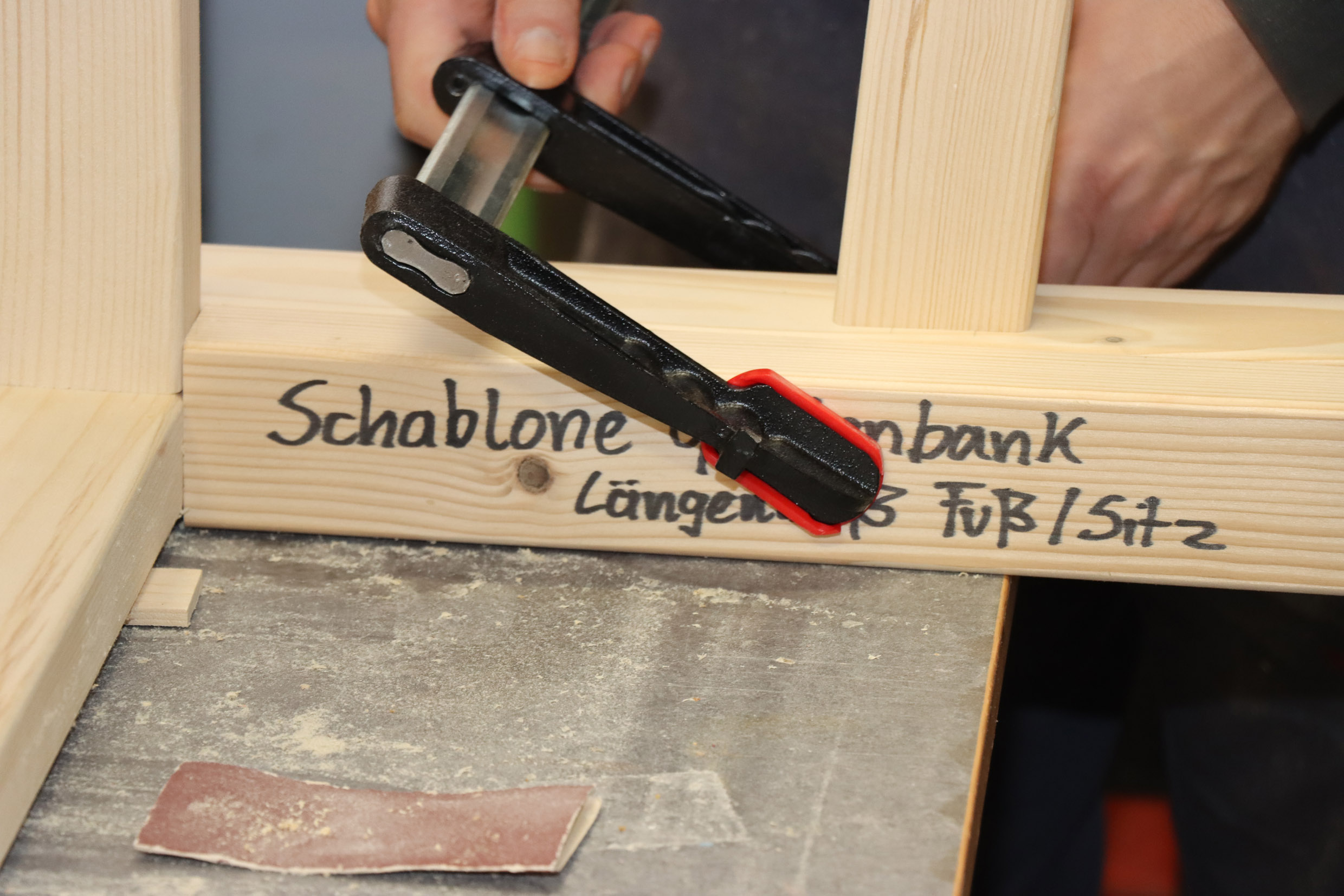 Eine Schraubzwinge drückt die Schablone an die Bank.