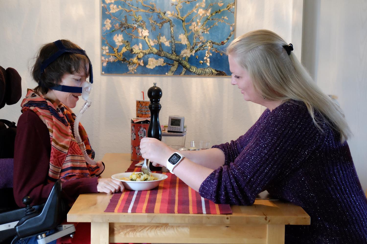 Eine Frau hilft einer Frau mit Behinderung beim Essen.