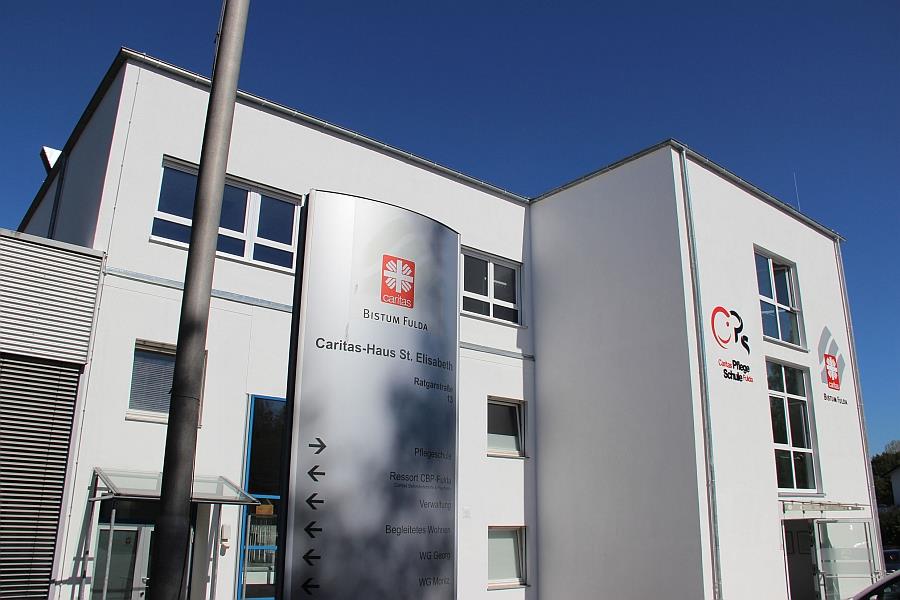 Wir sehen eine weiße Hausfront mit dem Logo der Pflegeschule