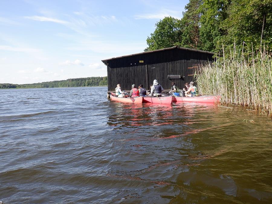 Vor einem Bootshaus schwimmen 3 Boote.