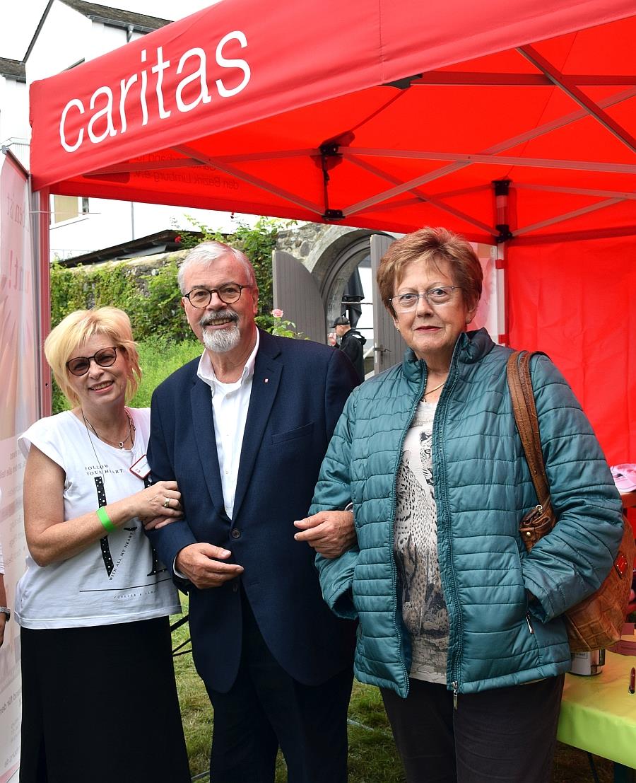 Drei Senioren stehen unter einem Caritas-Pavilion.