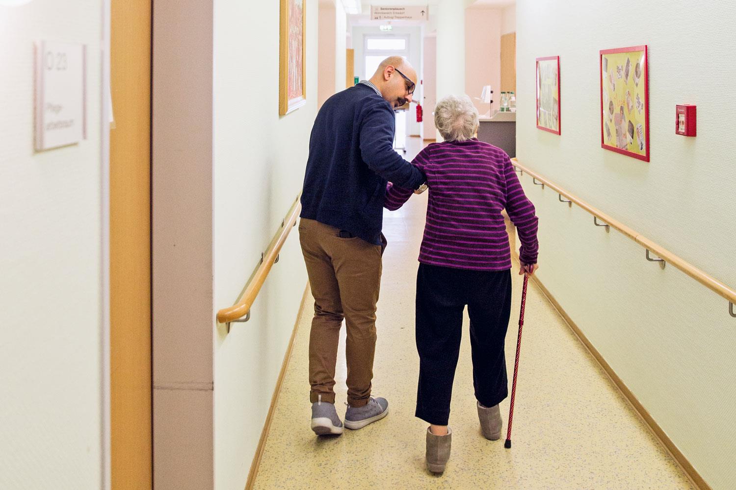 Medhi läuft mit einer Bewohnerin durch den Gang