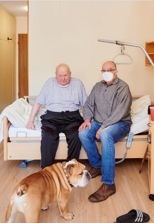 Ein Bewohner mit Besucher im Pflegezimmer - der Hund , ein Mops, ist mit dabei.