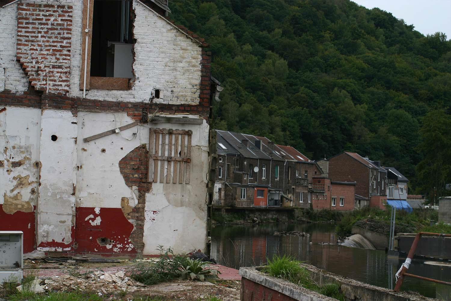 Man sieht ein ziemlich zerstörte Gebäude. Hinter dem Gebäude ist Fluss und und Häuser zu sehen. 
