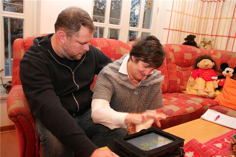Auf dem Foto sitzen Adrian Vallen und Carmen Wulf mit einem Computer auf dem Schoß auf dem Sofa