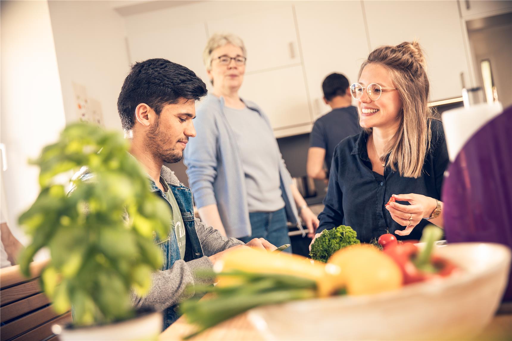 Das Foto zeigt junge Erwachsene, die gemeinsam Gemüse schneiden.